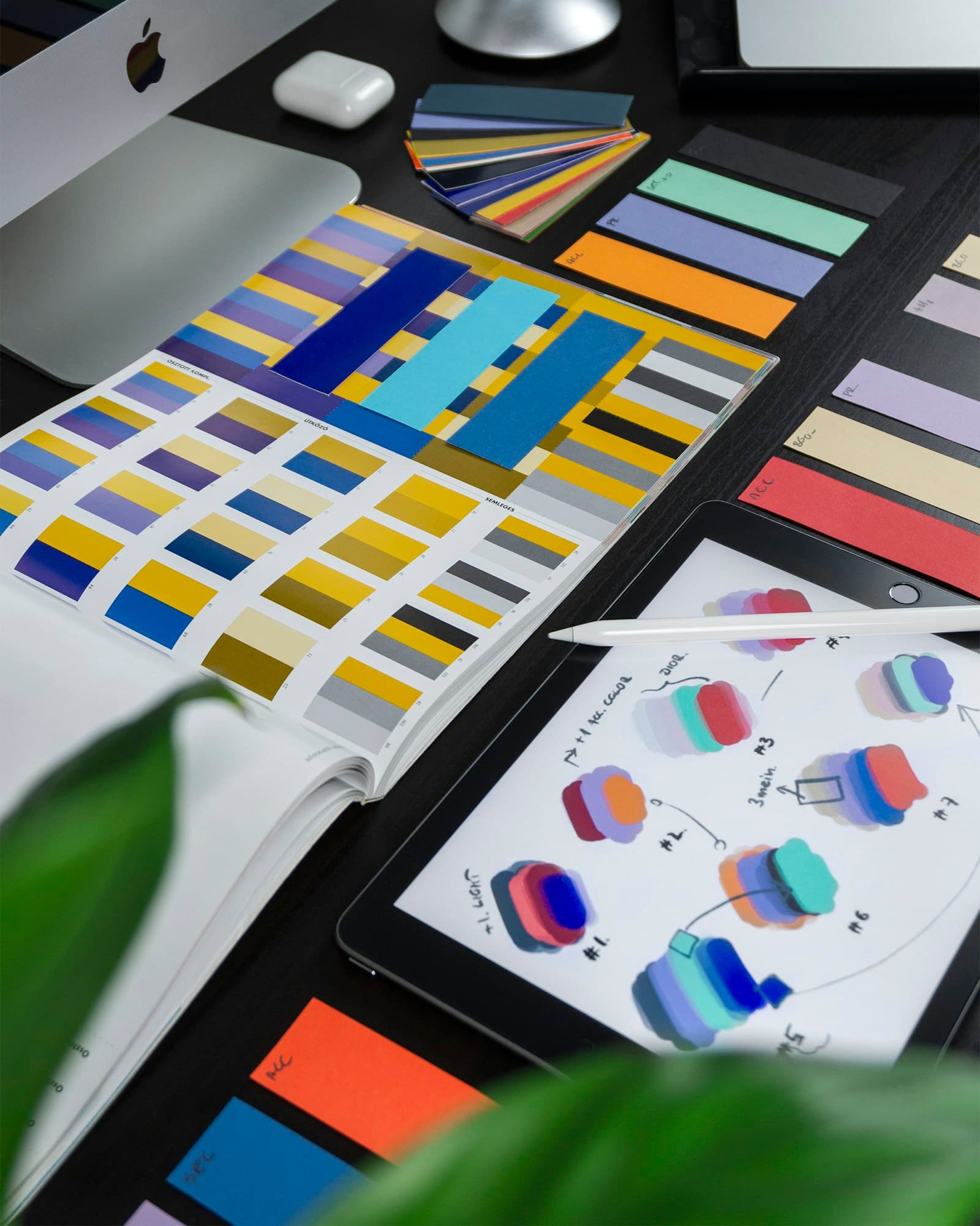Color swatches, a printed palette book, and a tablet of color studies on a dark desk