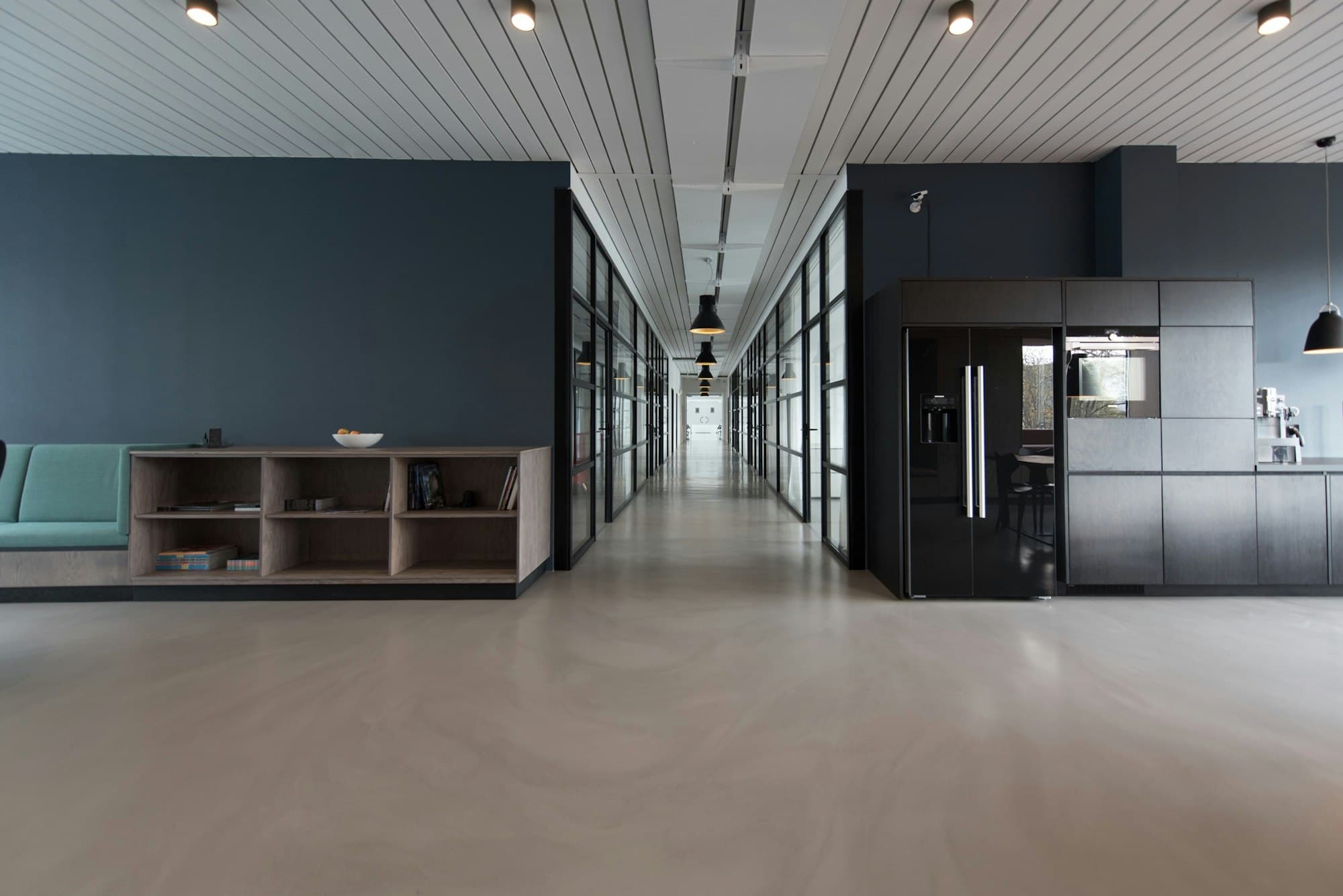 A long, quiet office corridor with glass rooms and a kitchen at the end