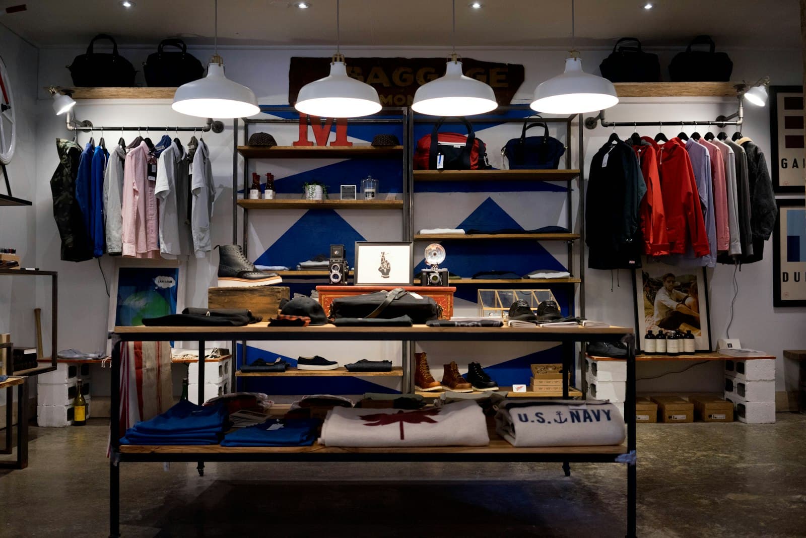 Independent clothing shop with wooden tables, hanging garments, bags, and warm pendant lights