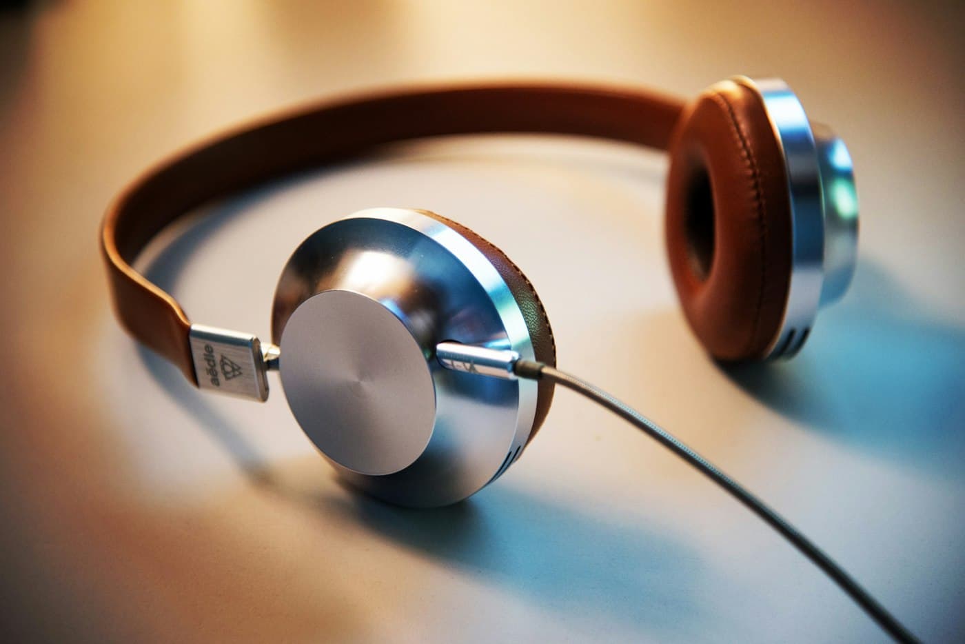 Silver and brown wired headphones with leather pads resting on a pale surface