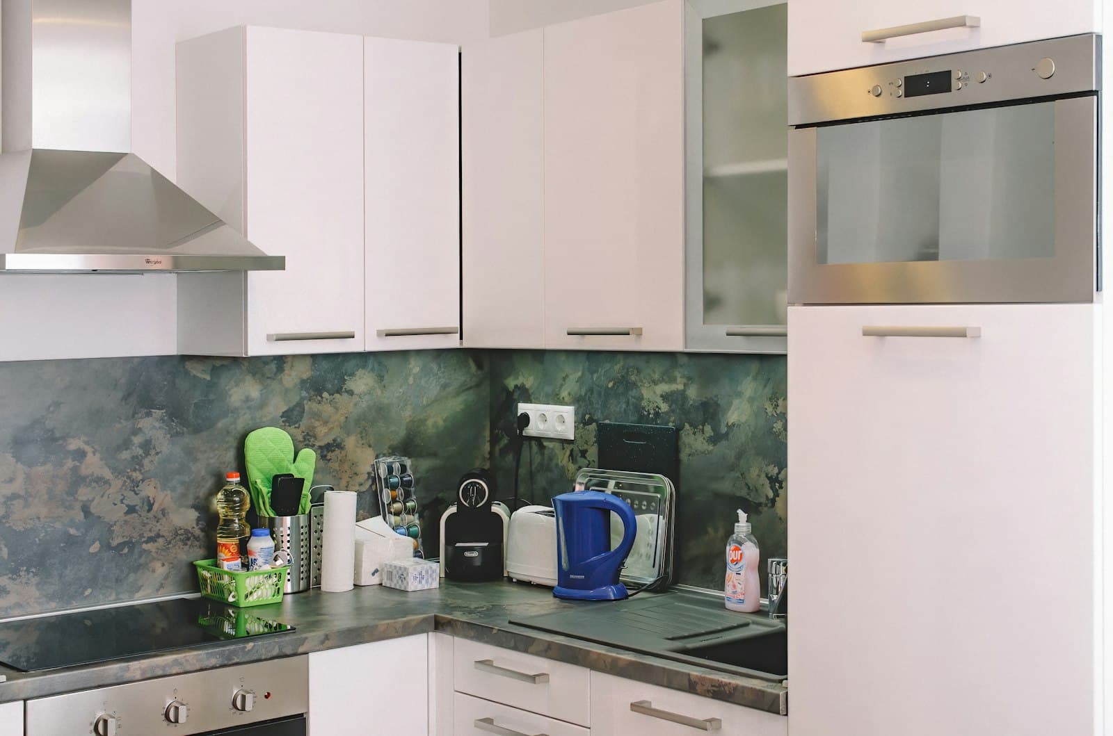 Compact white kitchen with a small blue electric kettle on a dark stone counter