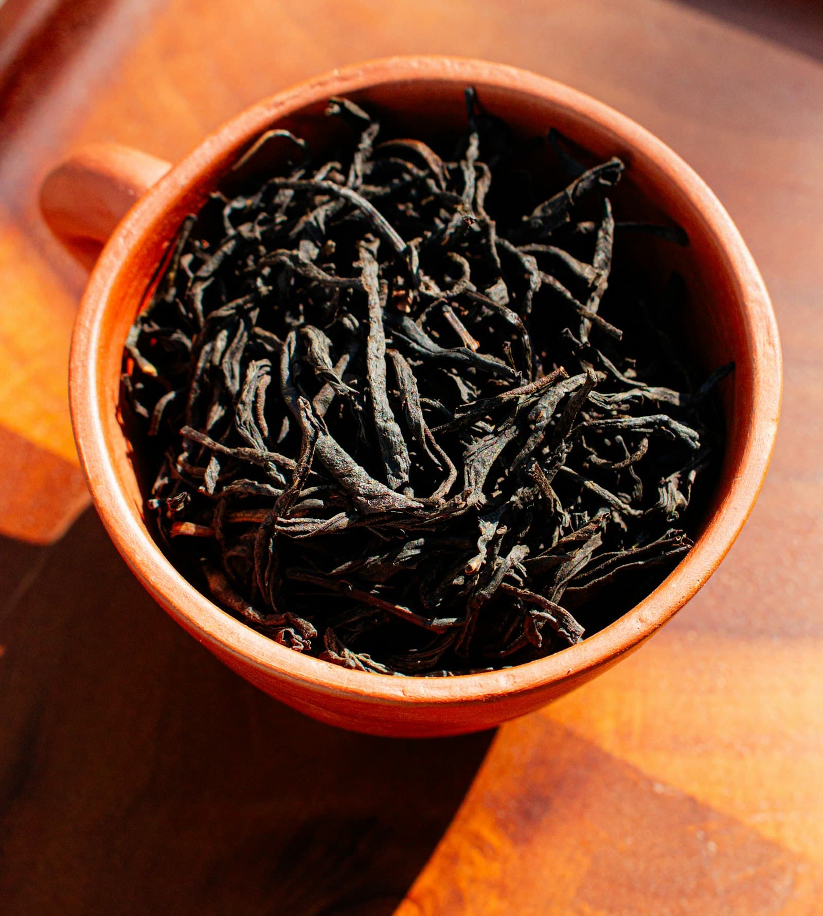 Long twisted black tea leaves filling a terracotta cup
